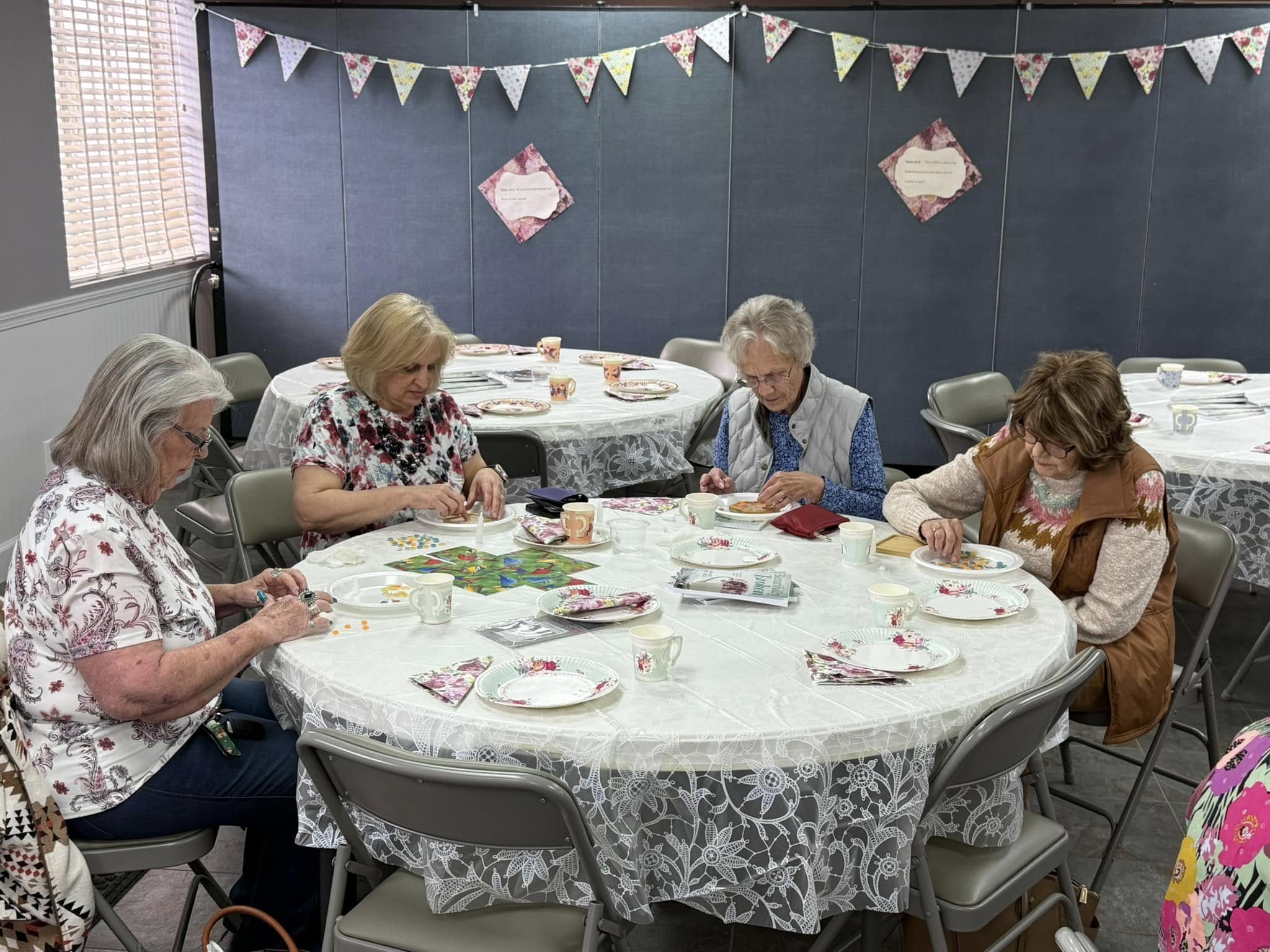Four women sit and make crafts with beads